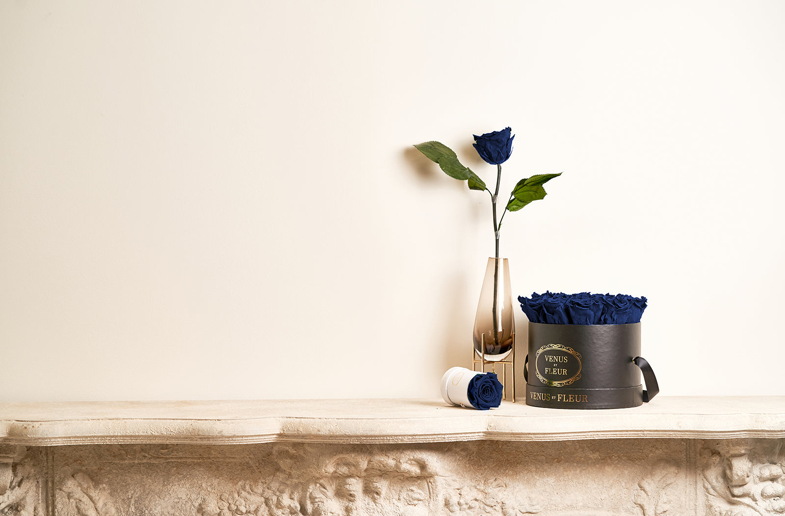 A vase with a single-stemmed dark blue rose and two flower box arrangements
