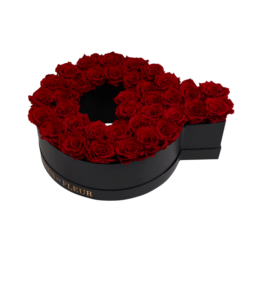 Black circular box filled with red roses arranged in a ring shape, with partial gold text 'VENUS ET FLEUR' visible on the side of the box.