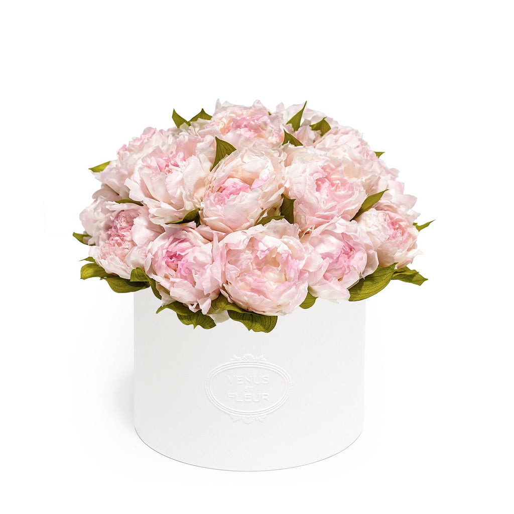 White round box with embossed text 'VENUS ET FLEUR' containing a bouquet of light pink peonies with green leaves.