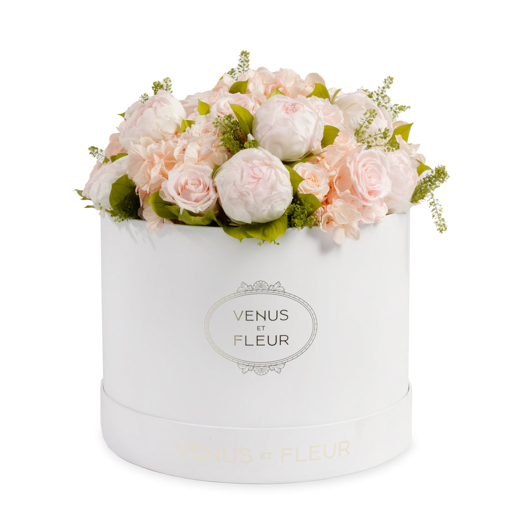 White round box filled with light pink roses and peonies with green leaves, labeled 'VENUS ET FLEUR'.