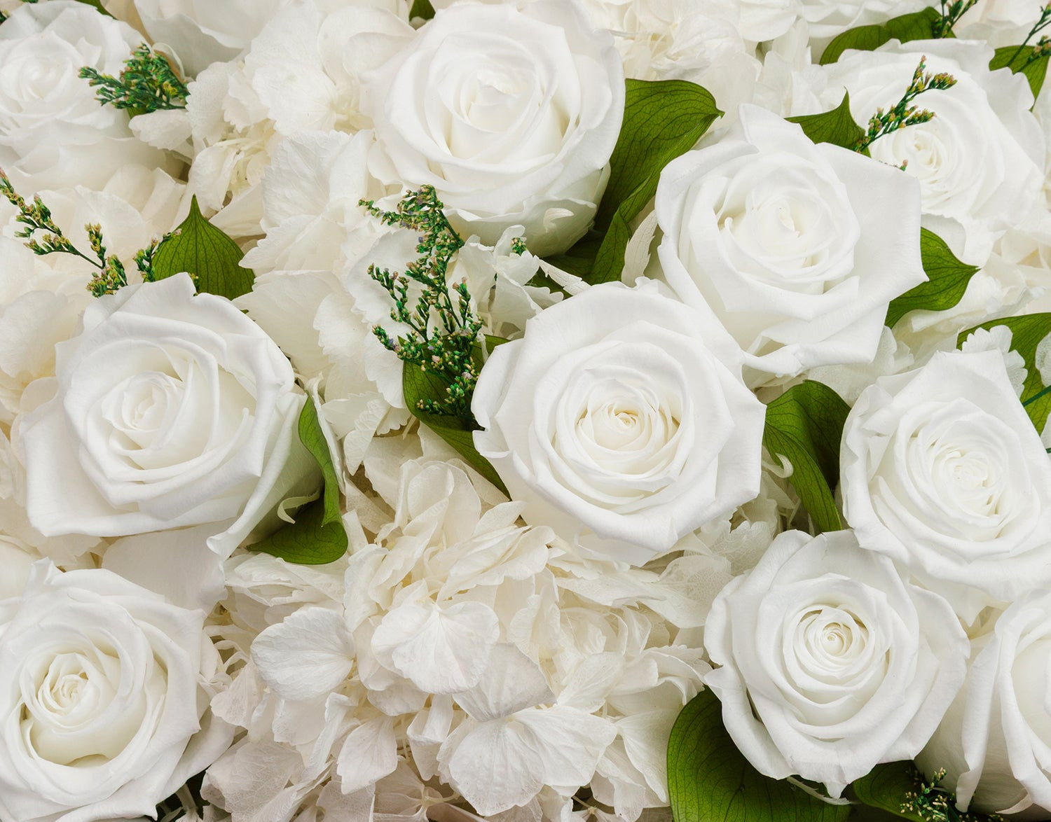 Close-up of white roses and white hydrangea flowers with green leaves arranged in a wooden basket.