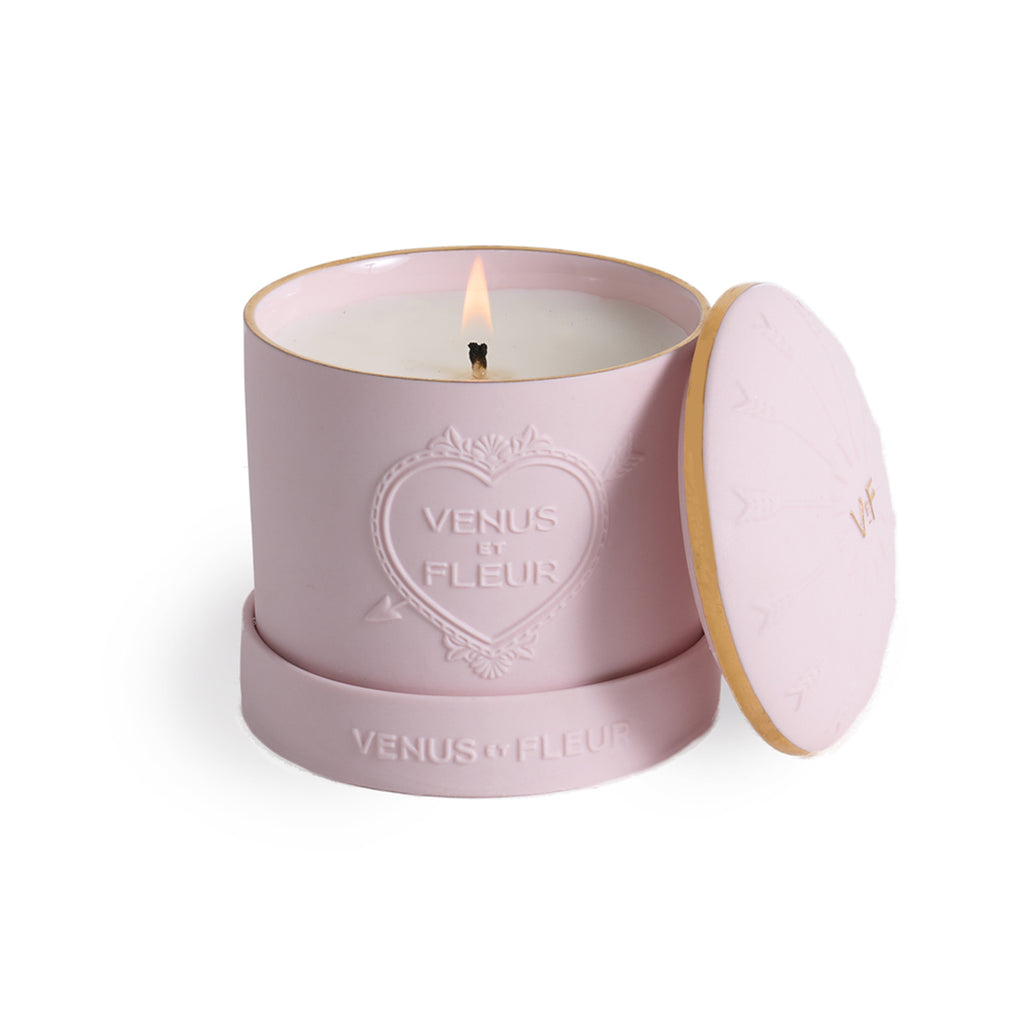 Pink lit candle in a round container with lid, embossed with a heart and text 'VENUS ET FLEUR' on the side and base