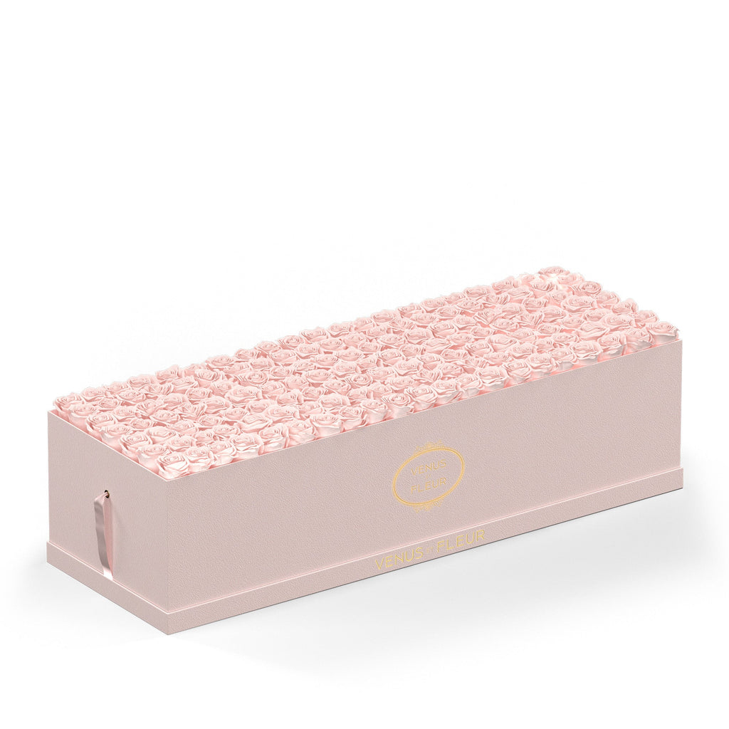 Rectangular pink box filled with light pink roses, with gold text 'VENUS FLEUR' on the side and front of the box.