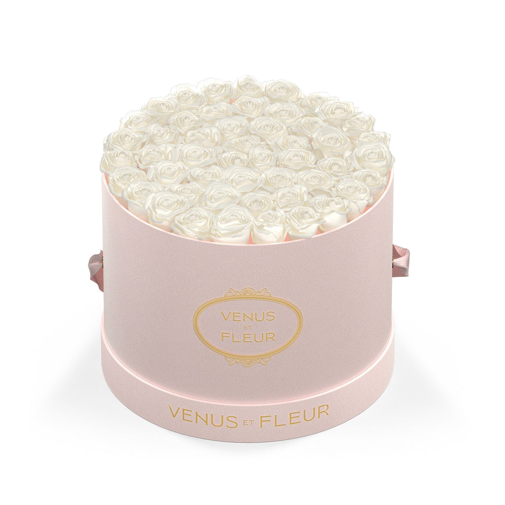 Round pink box filled with white roses, with 'VENUS ET FLEUR' written in gold on the box