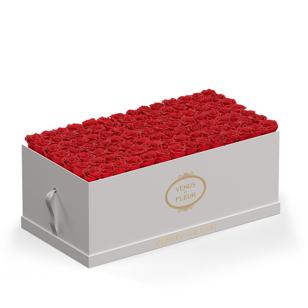 White rectangular box filled with red roses, with gold text 'VENUS ET FLEUR' on the front and side of the box.