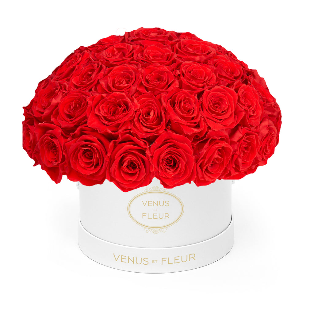 Round white box with many red roses arranged on top, labeled 'VENUS ET FLEUR'