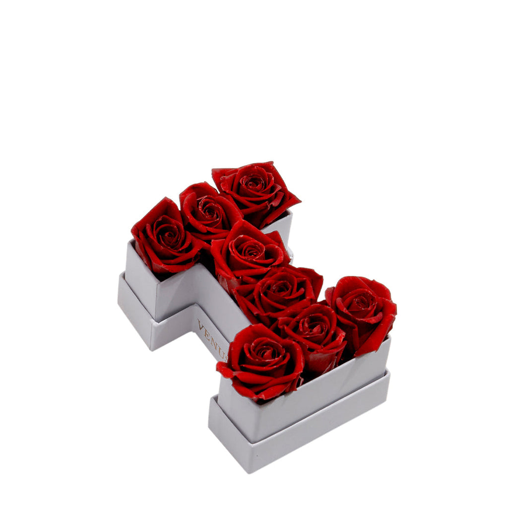 White box shaped like the letter 'I' filled with seven red roses, with the word 'VENUS' visible on the side of the box.