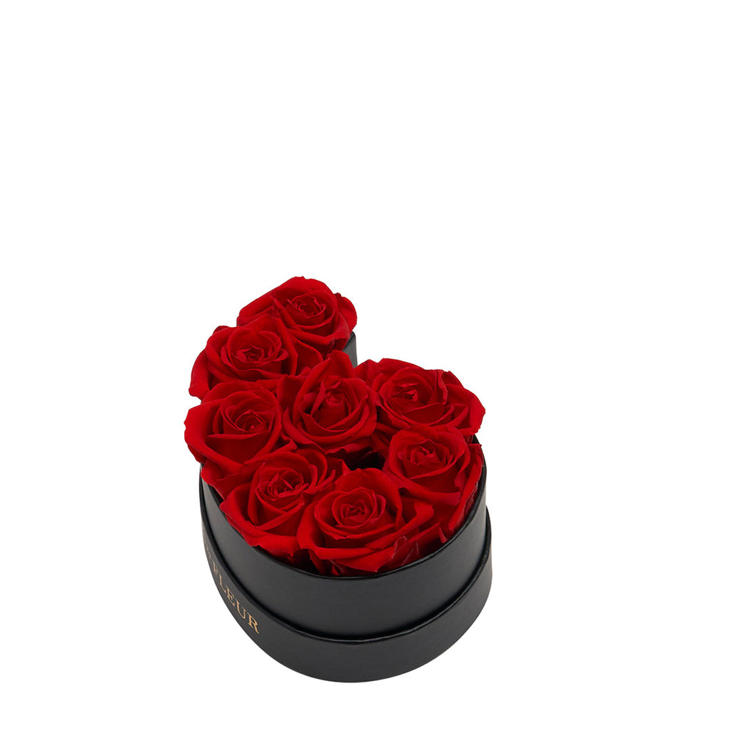 Black heart-shaped box containing six red roses