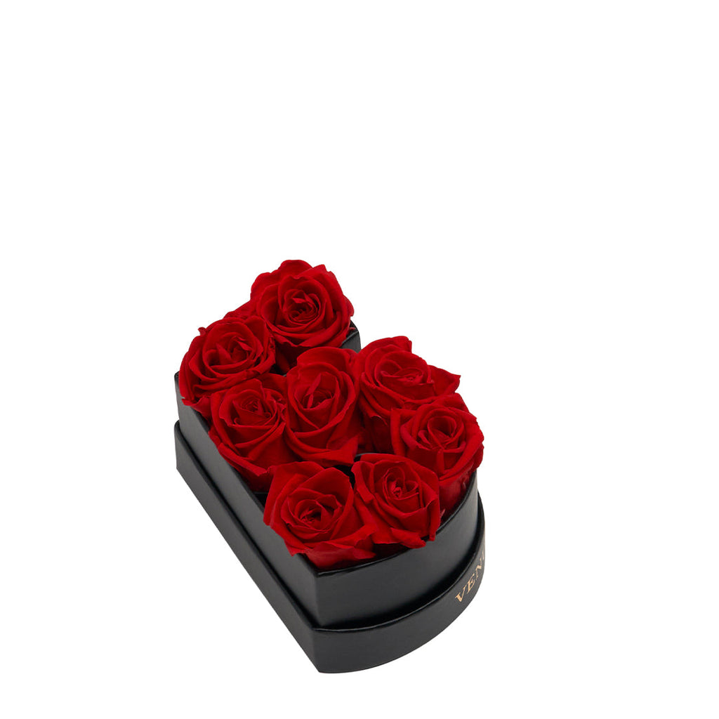 Black heart-shaped box containing eight red roses arranged closely together